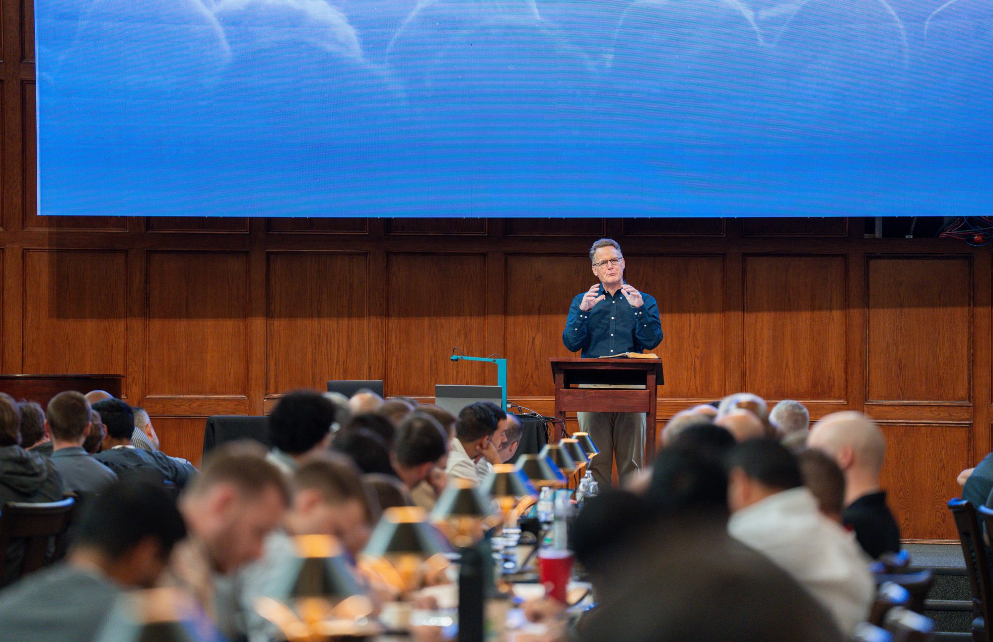 Steven Smith teaching from a lectern at the front of a wood-paneled library hall, with pastors seated at long tables